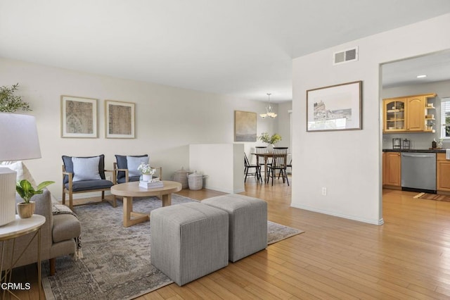 living area featuring a chandelier, light wood finished floors, visible vents, and baseboards