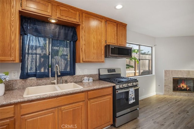 kitchen featuring sink, light hardwood / wood-style floors, stainless steel gas range oven, and a fireplace