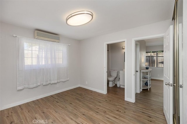 unfurnished bedroom featuring ensuite bathroom, wood-type flooring, and a wall unit AC