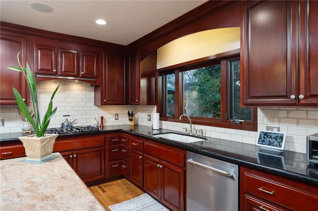 kitchen featuring appliances with stainless steel finishes, light hardwood / wood-style flooring, dark stone counters, backsplash, and sink