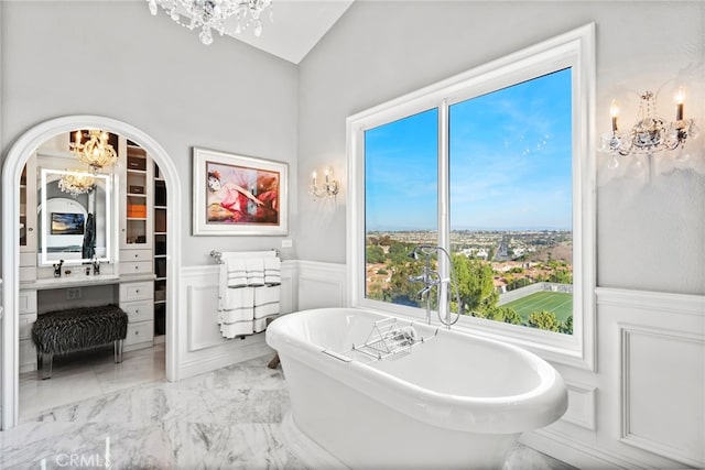 bathroom featuring a freestanding tub, wainscoting, a decorative wall, marble finish floor, and a chandelier