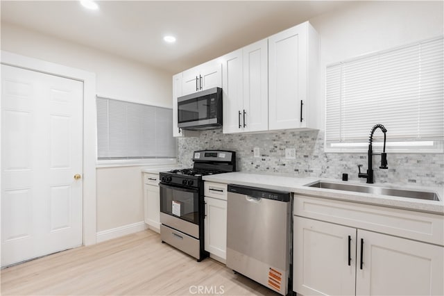 kitchen featuring sink, light wood-type flooring, stainless steel appliances, white cabinets, and tasteful backsplash