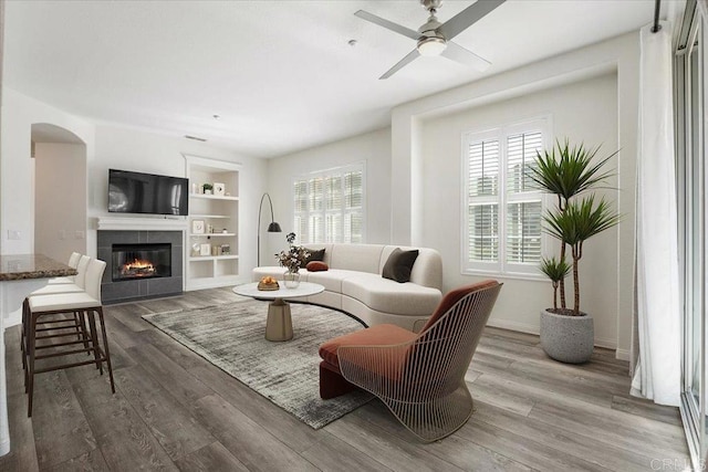 sitting room featuring ceiling fan, wood-type flooring, built in features, and a fireplace