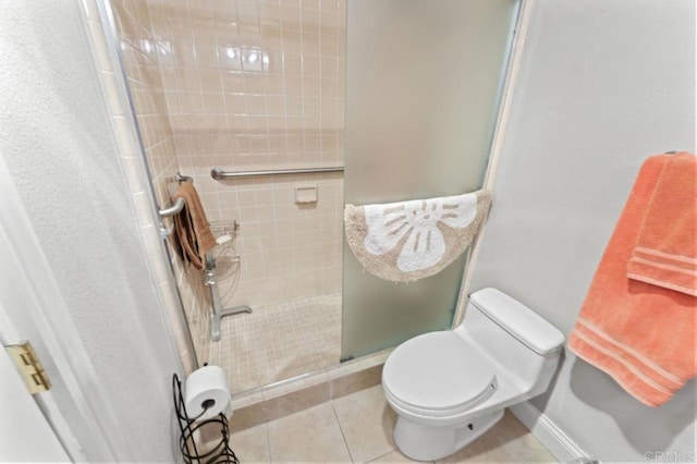 bathroom featuring toilet, a shower stall, baseboards, and tile patterned floors