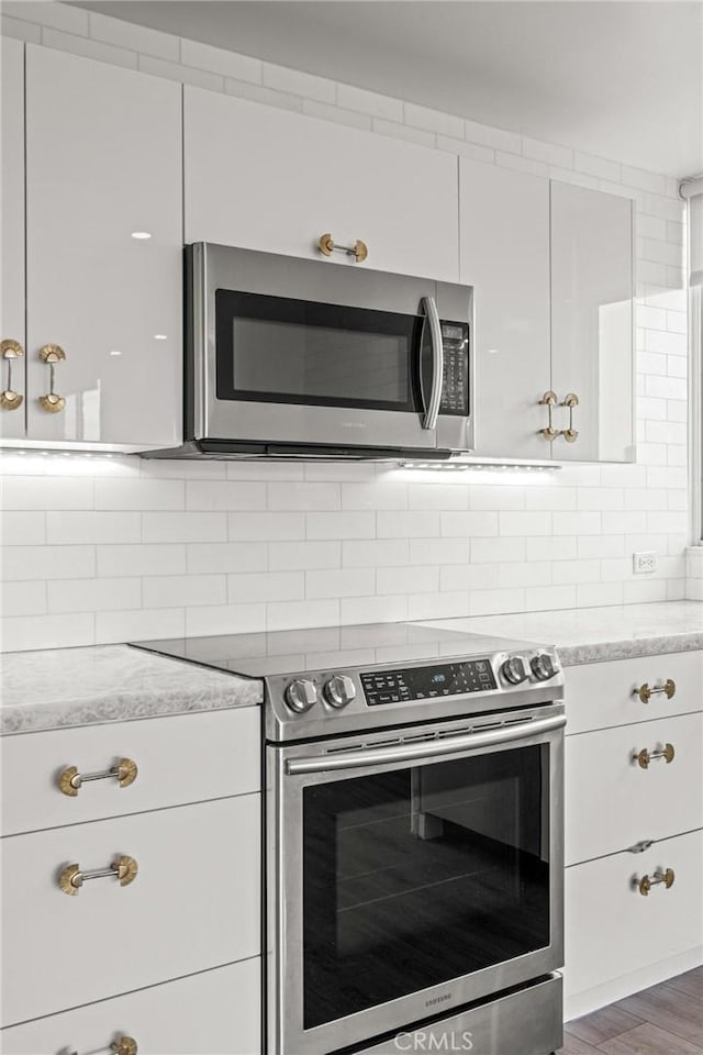 kitchen featuring appliances with stainless steel finishes, light stone countertops, white cabinets, decorative backsplash, and dark hardwood / wood-style flooring