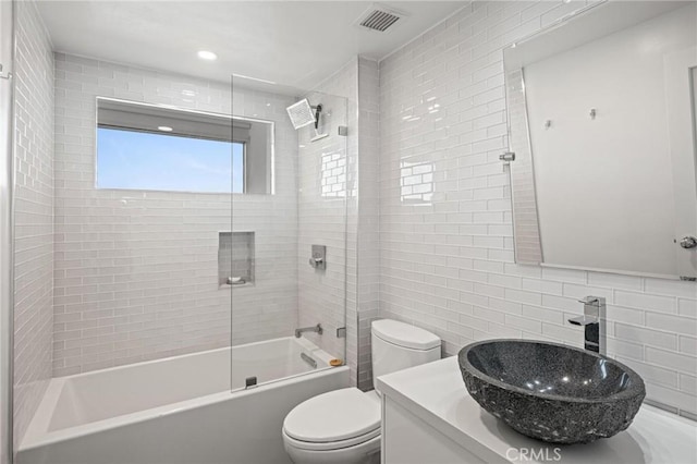 full bathroom with tiled shower / bath combo, toilet, tile walls, backsplash, and vanity