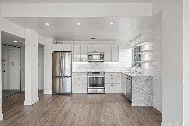 kitchen with stainless steel appliances, light hardwood / wood-style floors, backsplash, sink, and white cabinetry