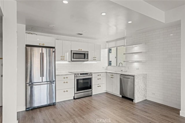 kitchen featuring appliances with stainless steel finishes, sink, light hardwood / wood-style floors, white cabinets, and decorative backsplash