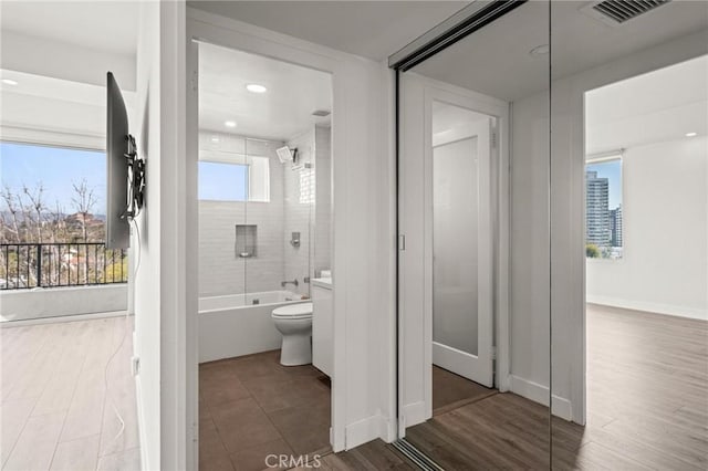 bathroom featuring hardwood / wood-style flooring, tiled shower / bath, and toilet