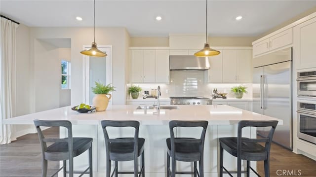 kitchen with sink, appliances with stainless steel finishes, a kitchen island with sink, and white cabinetry