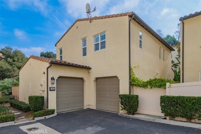 view of side of property with a garage, a tiled roof, aphalt driveway, and stucco siding