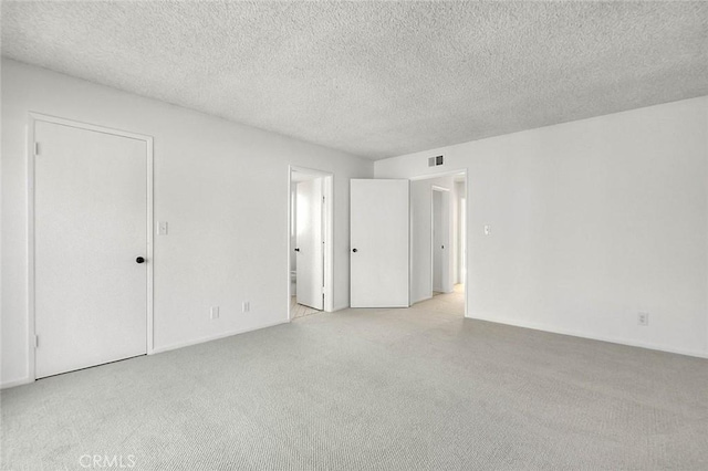 unfurnished room featuring visible vents, light colored carpet, and a textured ceiling