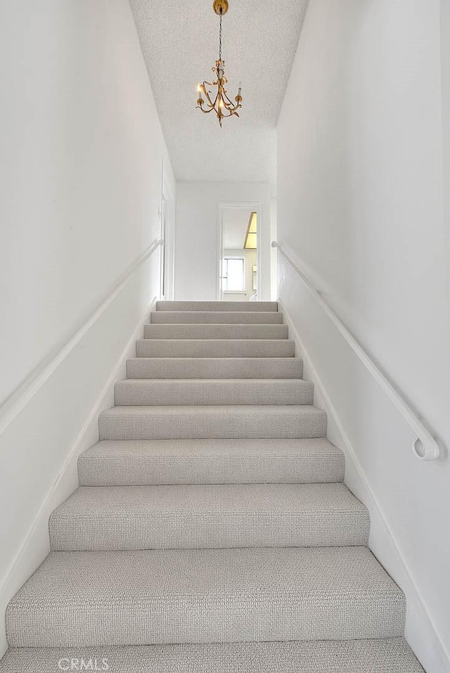 stairs featuring a notable chandelier and a textured ceiling