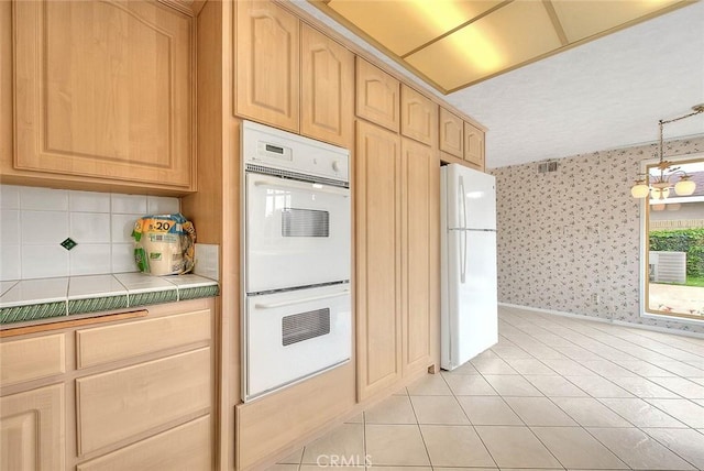 kitchen featuring light brown cabinets, wallpapered walls, tile countertops, light tile patterned flooring, and white appliances