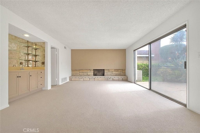 spare room with visible vents, light colored carpet, a stone fireplace, a textured ceiling, and a sink