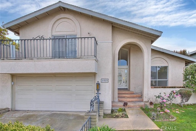 view of front of home with stucco siding, a balcony, concrete driveway, and an attached garage