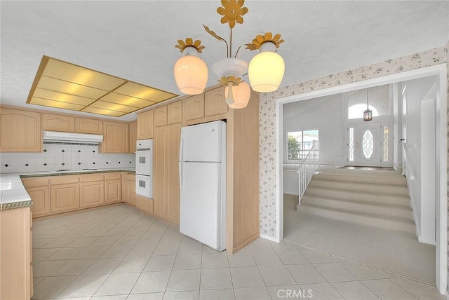 kitchen with white appliances, wallpapered walls, light brown cabinetry, light countertops, and under cabinet range hood