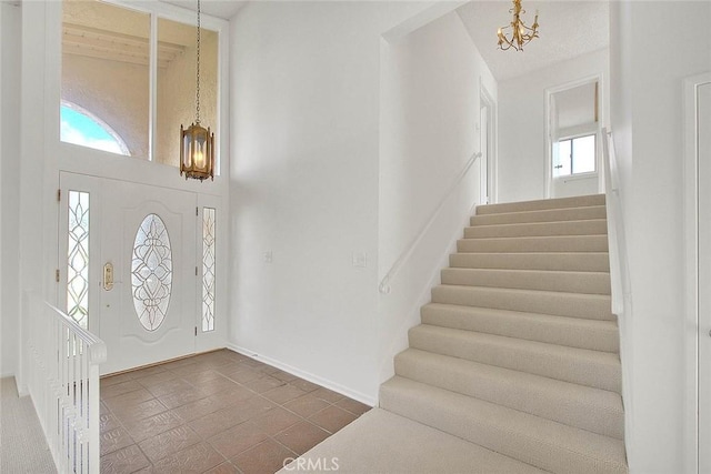 entrance foyer with stairway, a notable chandelier, baseboards, and a towering ceiling