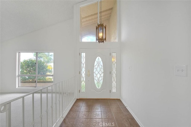 entryway with dark tile patterned floors, high vaulted ceiling, and baseboards