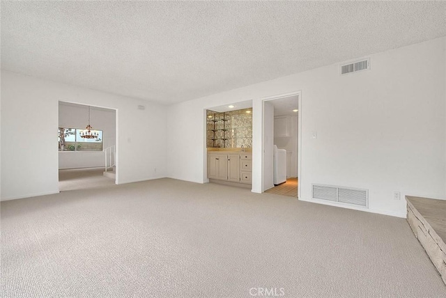 unfurnished bedroom featuring a textured ceiling, connected bathroom, visible vents, and light carpet