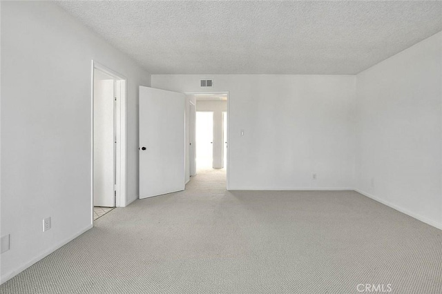 spare room with light colored carpet, visible vents, and a textured ceiling