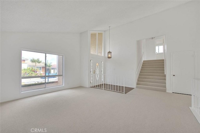 unfurnished living room with carpet floors, a textured ceiling, lofted ceiling, and stairs