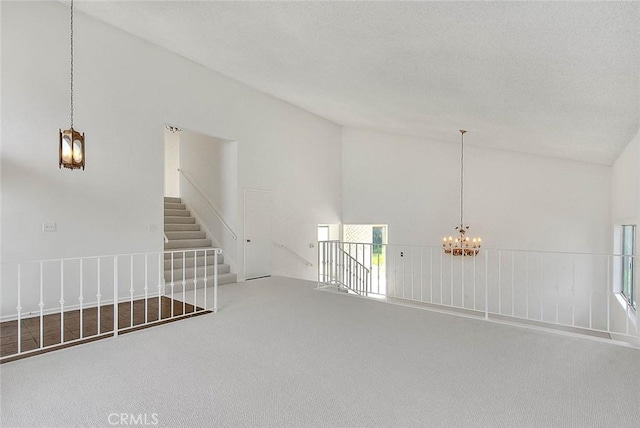 unfurnished room featuring carpet, high vaulted ceiling, stairs, an inviting chandelier, and a textured ceiling