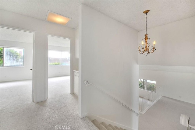 corridor with an inviting chandelier, an upstairs landing, light colored carpet, and a textured ceiling