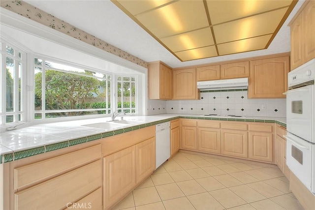 kitchen featuring a sink, white appliances, under cabinet range hood, and light brown cabinetry