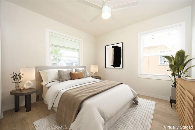 bedroom featuring ceiling fan, baseboards, light wood-style floors, and multiple windows