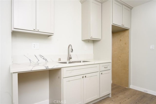 kitchen with a sink, light wood-style floors, light stone countertops, and white cabinetry