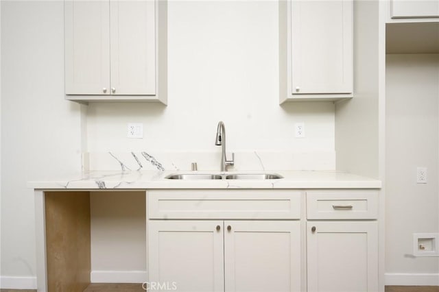 kitchen featuring light stone countertops, white cabinetry, and a sink