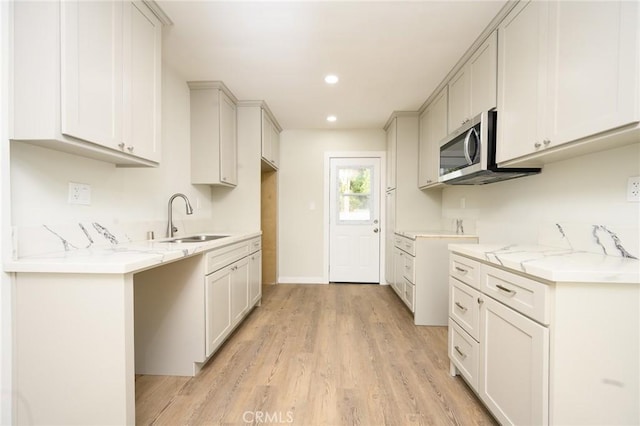 kitchen with light stone counters, white cabinets, a sink, and stainless steel microwave