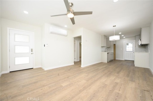 unfurnished living room featuring an AC wall unit, light wood finished floors, recessed lighting, and baseboards