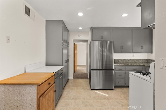 kitchen featuring gray cabinets, stainless steel refrigerator, and white gas range oven