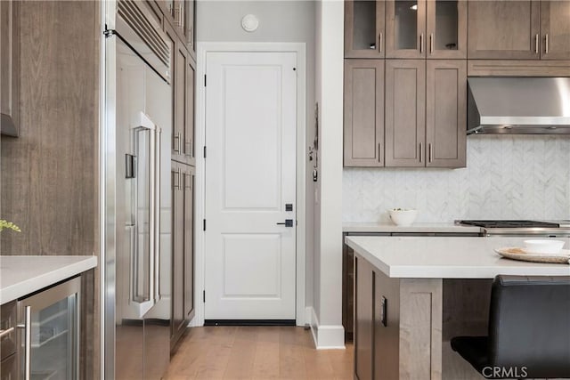 kitchen with decorative backsplash, light hardwood / wood-style flooring, wall chimney range hood, and wine cooler