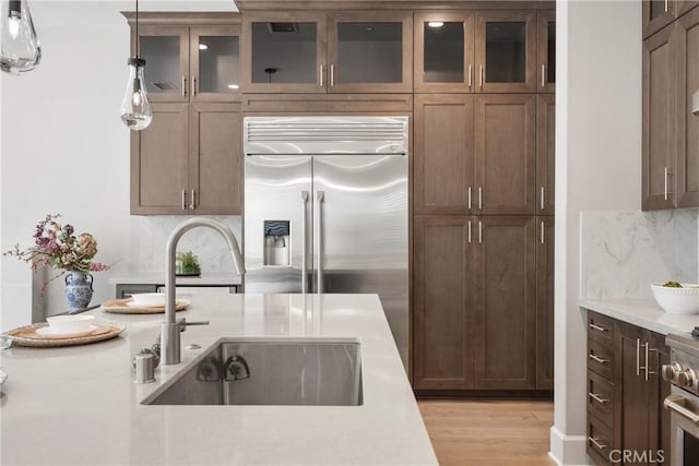 kitchen featuring sink, light wood-type flooring, built in refrigerator, decorative light fixtures, and decorative backsplash