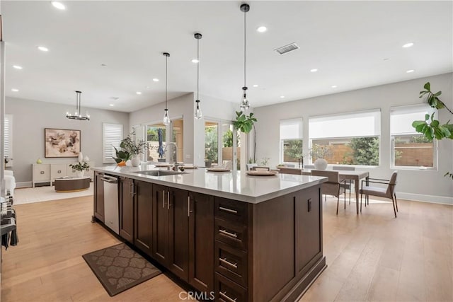 kitchen with a center island with sink, hanging light fixtures, dark brown cabinetry, light hardwood / wood-style floors, and sink