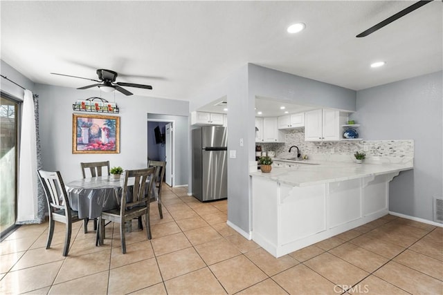 kitchen with white cabinetry, ceiling fan, kitchen peninsula, stainless steel refrigerator, and tasteful backsplash