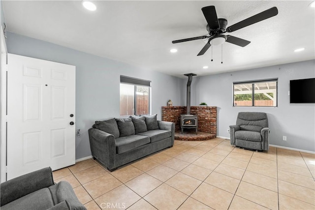 tiled living room featuring ceiling fan, a wood stove, and a wealth of natural light