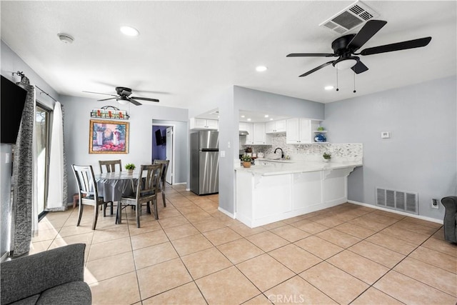 kitchen with kitchen peninsula, stainless steel refrigerator, backsplash, light tile patterned floors, and white cabinets