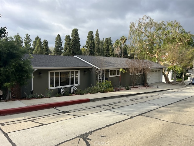 ranch-style house featuring concrete driveway, a garage, roof with shingles, and stucco siding