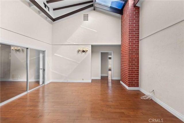 interior space featuring a skylight, baseboards, visible vents, wood finished floors, and high vaulted ceiling