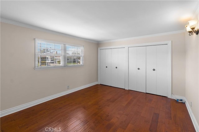 unfurnished bedroom featuring two closets, crown molding, baseboards, and wood finished floors