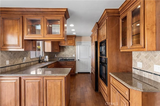 kitchen with stone counters, brown cabinets, a sink, a peninsula, and black appliances