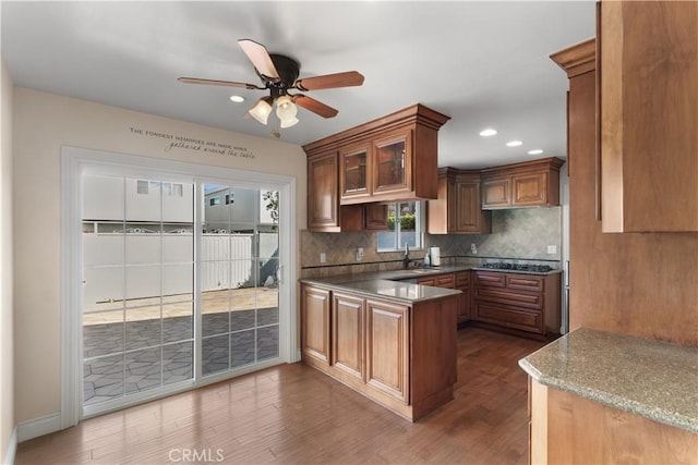 kitchen with dark wood-style floors, stainless steel gas cooktop, decorative backsplash, glass insert cabinets, and a peninsula