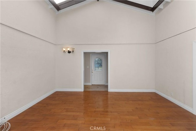 spare room with high vaulted ceiling, wood finished floors, and baseboards