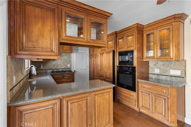 kitchen featuring dark wood finished floors, brown cabinetry, stone counters, black appliances, and a sink