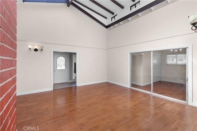 interior space with baseboards, high vaulted ceiling, beam ceiling, and wood finished floors