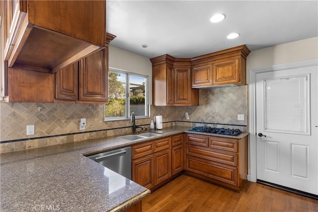 kitchen with black gas cooktop, stainless steel dishwasher, light wood-style floors, brown cabinetry, and a sink